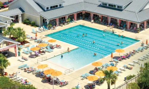 Aerial view of a resort-style community pool with lap lanes, lounge chairs, yellow umbrellas, and a clubhouse.