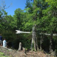 Boys fishing on river bank with boat driving by