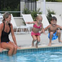 Children jumping into the pool next to their mom